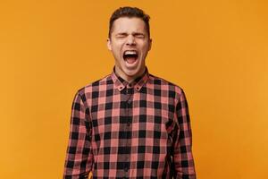 Angry, irate man, with mouth opened in a shout isolated over yellow background. A manager who can no longer restrain his emotions, tired of problems at work went into a separate room and shouted. photo