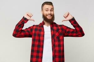 Happy portrait of a cheerful glad joyful proud bearded man in checkered shirt clenching fists and pointing thumbs on himself like winner with eyes closed in pleasure, isolated over white background photo
