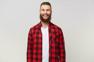 estudio Disparo de emocionado gracioso joven atractivo barbado hombre, vestido en camisa, tiene contento alegre cara expresión, sonriente, riendo aislado en blanco antecedentes foto