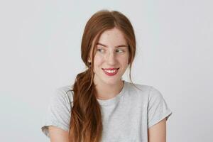 Closeup of smiling pretty redhead young woman with freckles wears gray t shirt feels happy and looks to the side isolated over white background photo