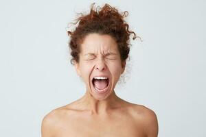 Horizontal shot of crazy hysterical young woman with curly hair and soft healthy skin close eyes and screaming isolated over white background Looks stressed and feels angry photo