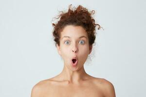 Close up shot of amazed cute curly young woman with perfect healthy skin looks shocked and surprised isolated over white background Feels excited after shower photo