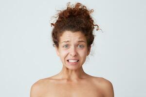 Close up shot of upset worried young woman with curly hair and healthy skin after applying mask or cream feels confused and embarrassed isolated over white background photo