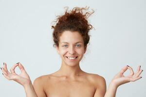 Horizontal shot of happy peaceful yong woman with perfect skin after applying cream or mask shows meditation gesture by hands isolated over white background Feels peaceful and satisfied photo