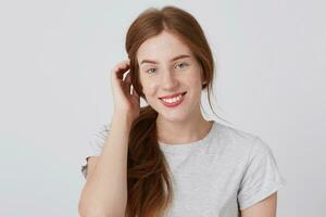 Portrait of smiling cute redhead young woman with long hair and freckles looks satisfied and feels happy isolated over white background Looks directly in camera photo