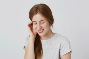 Closeup of happy shy young woman with long red hair and freckles smiling and feels embarrassed isolated over white background Looks down photo