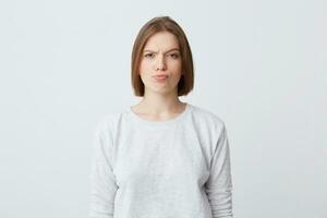 Portrait of serious unhappy young woman in long-sleeve standing and frowning her face isolated over white background Looking directly in camera photo