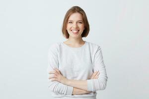 Portrait of cheerful attractive young woman in long-sleeve standing with arms crossed and smiling isolated over white background Looks confident photo