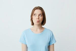 Closeup of thoughtful beautiful young woman in blue t shirt standing and thinking about her future job looking to the side isolated over white background photo