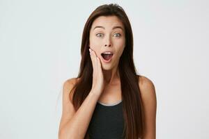 Surprised attractive young woman with long hair and opened mouth touching her cheek looking amazed and excited isolated over white background photo