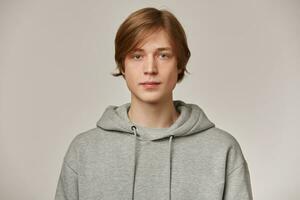 grave mirando masculino, hermoso chico con rubio cabello. vistiendo gris sudadera. personas y emoción concepto. acecho confidente a el cámara aislado terminado gris antecedentes foto