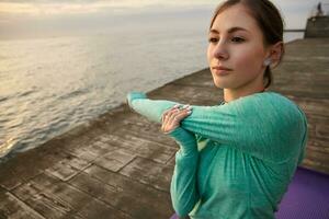 retrato de joven deportivo dama en brillante deporte viste, hace Mañana extensión, trenes a el playa, siente bueno y disfrutar el Mañana. salud cuidado concepto. foto