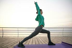 Delgado deportivo joven mujer en yoga pose, vestido deporte lleva. bien conformado joven niña trenes a el playa, hace Mañana extensión. salud cuidado concepto. foto