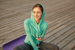 Photo of young girl in bright sportswear, listening cool playlist on headphones after morning yoga and enjoy the sun. Health care concept.