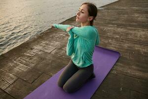 Portrait of sporty young woman in bright sport wears, makes morning stretching in yoga pose, trains at the seaside. Health care concept. photo