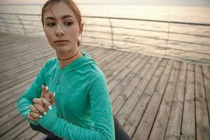 Health care concept. Photo of slim sporty young woman in yoga pose, wears in sportwears, trains at the seaside, makes morning stretching.