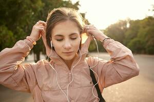 Young dreaming woman walking at the park and listening favorite romantic song on headphones, feels great and enjoy the day. photo