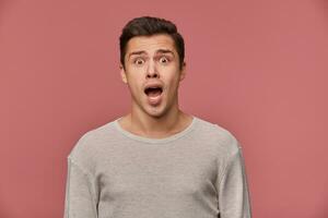 Young handsome shocked man in blank long sleeve, looks at the camera with with wide open mouth in surprised expression, isolated over pink background. photo