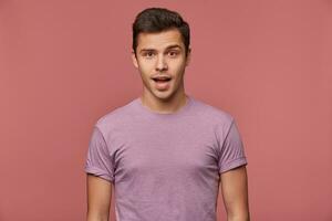 foto de hermoso alegre chico usa en blanco camiseta, mira a el cámara con contento expresión, soportes terminado rosado antecedentes.