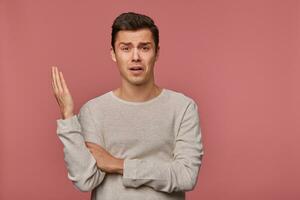 Portrait of young indigant guy wears in blank long sleeve, looks at the camera with surprised expression, looks shocked, isolated over pink background. photo