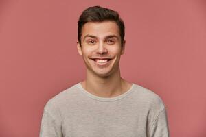 retrato de hermoso joven alegre hombre usa en blanco largo manga, mira a el cámara con contento expresiones, soportes terminado rosado antecedentes. foto