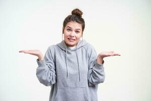 Portrait of bewildered young blue-eyed brown haired lady frowning forehead and shrugging with raised palms while posing over white background in sporty clothes photo