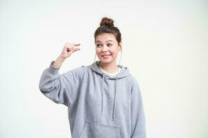 Confused young lovely long haired female with natural makeup looking ironically on her hand while showing small size with her fingers, isolated over white background photo