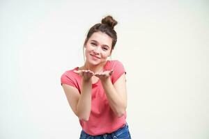 Horizontal shot of lovely young brunette female with palms up looking positively at camera with charming smile while standing against white background photo