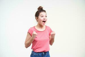 Overjoyed young lovely brunette lady keeping her mouth opened while screaming and raising emotionally her hands while rejoicing about something, isolated over white background photo