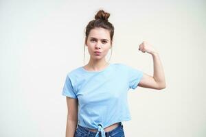 Serious young pretty dark haired woman with natural makeup squinting her eyes while looking at camera and raising hand, isolated over white background photo