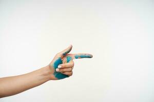 Cropped photo of lady's hand with blue paint on it being raised while pointing ahead with index finger, being isolated over white background