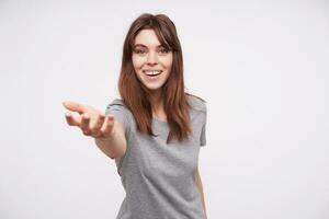 Happy young attractive long haired brunette female with natural makeup pulling to somebody raised hand and smiling cheerfully while standing over white background photo