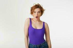 Young surprised attractive short-haired girl, wearing a purple jersey, looking at the camera in surprise with wide open mouth and eyes, she heard the shocking news. Isolated over white wall. photo