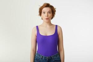 Portrait of a young happy amazed attractive short-haired girl, wearing a purple jersey, looking at the camera and speaks lips wow isolated over white wall. photo