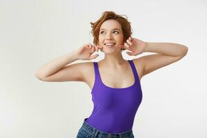 Portrit of a young happy fabulous short-haired girl, wearing a purple jersey, smiling broadly, holds hands at the face and shows natural beauty, isolated over white background. photo