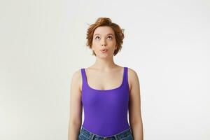 appy amazed young attractive short-haired girl, wearing a purple jersey, amazed looking up at the copy space, speaks lips wow isolated over white wall. photo