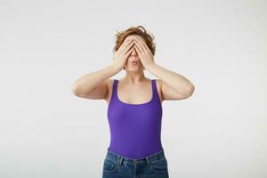 Happy amazed young attractive short-haired girl covers her eyes with hands going to see surprise prepared by her boyfriend. Young cheerful lady covering her face with hands stands over white wall. photo