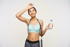 Studio photo of young positive brunette woman without makeup holding raised palm on her forehead while relaxing after fitness class, isolated over white background