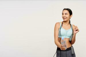 Pleased young attractive brown haired lady with ponytail hairstyle looking cheerfully aside while preparing for morning workout, isolated over white background photo