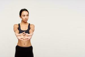 Good looking young lovely sporty dark haired woman without makeup making exercises for her hands while standing over white background in sporty clothes photo