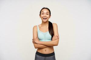 Teenage sporty girl, happy looking asian woman with dark long hair. Wearing sportswear and have a big smile, holds arms crossed on a chest. Watching at the camera isolated over white background photo