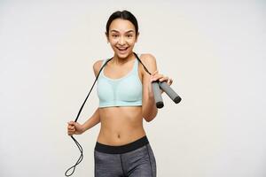 Teenage girl, sporty looking asian woman with dark long hair. Wearing sportswear and holding a jump rope over her neck. Happy to exercise. Watching at the camera isolated over white background photo