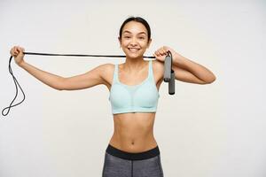 Portrait of cute, sporty asian girl with dark long hair. Wearing sportswear and stretching a jump rope over her neck. Happy for action. Watching smile at the camera isolated over white background photo