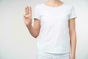 Studio photo of young woman keeping hand raised and forming letter w while standing over white background. Sign language and human hands concept