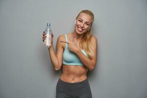 Cheerful sporty young blonde woman with long hair keeping bottle of water in hand photo