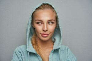 Pleasant looking young smiling blonde female with natural makeup posing over light grey background photo