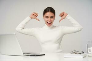 Excited young pretty dark haired woman showing on herself with raised hands and looking joyfully at camera with wide mouth opened, isolated over white background in formal clothes photo