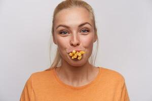 Close-up of funny attractive young blonde female with casual hairstyle looking joyfully at camera and having mouth full of french fries, fooling with food while posing over white background photo