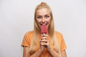 emocionado de ojos azules bonito joven largo peludo rubia dama alegría acerca de sabroso helado ella es saboreo y mirando asombrado a cámara, en pie en contra blanco antecedentes foto