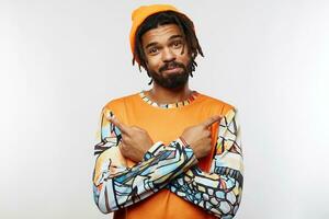 Portrait of positive young bearded dark skinned guy crossing hands with raised forefingers on his chest while looking at camera with pleasant smile, standing over white background photo